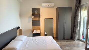 A hotel room with a bed, a wardrobe, a mirror, and a window with curtains.