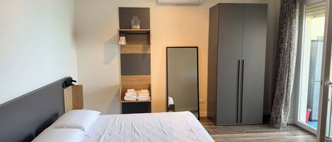 A hotel room with a bed, a wardrobe, a mirror, and a window with curtains.
