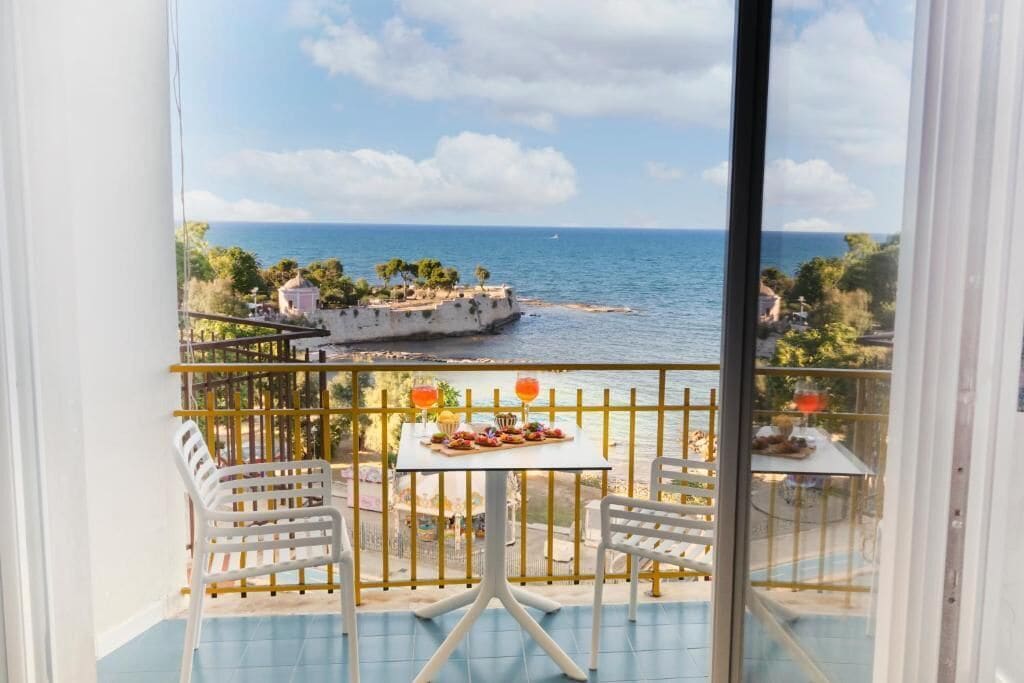 Un balcón con vista al mar, una mesa con comida y dos sillas.