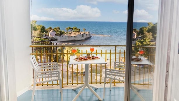 Een balkon met uitzicht op zee, een tafel met eten en twee stoelen.
