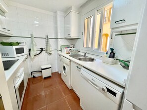 A compact kitchen with a washing machine, microwave, and sink. - Alcaraván T3 - Ref.12 (Isla Canela)