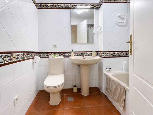 Et badeværelse med toilet, vask og badekar.