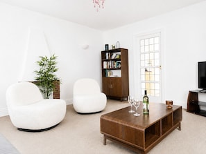 Una sala de estar moderna con dos sillones blancos, una mesa de centro de madera, una estantería y un televisor.