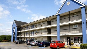 Um motel de vários andares com uma mesa de recepção, estacionamento e um cão passeando lá fora.