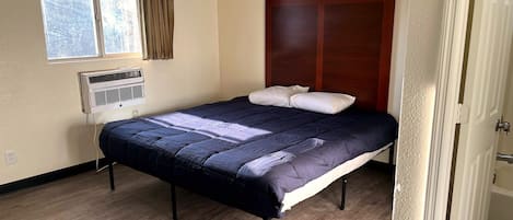 A single bed with a dark-colored headboard, a window with curtains, and a wall-mounted air conditioning unit.