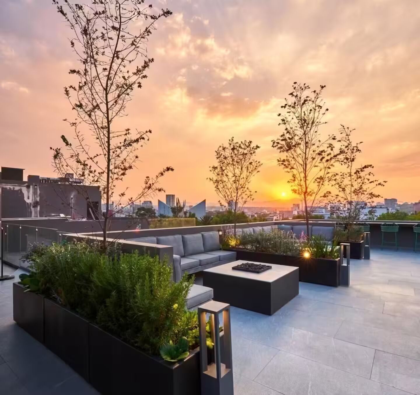 Een terras op het dak met buitenmeubels, plantenbakken en uitzicht op een zonsondergang.