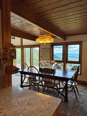 A dining area with a wooden table and chairs, a hanging light fixture, and large windows offering a view of the outdoors. - 6-bedroom mountain home with expansive views in Meadows of Dan, VA (Meadows of Dan)