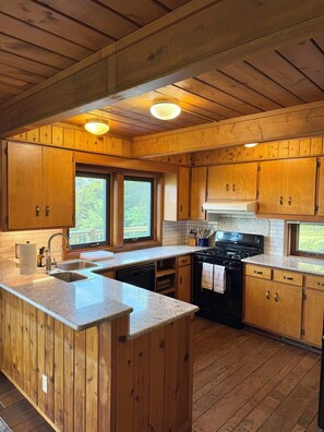 A kitchen with wooden cabinets, a central island, a stove, and a window. - 6-bedroom mountain home with expansive views in Meadows of Dan, VA (Meadows of Dan)