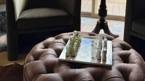 A room with a fireplace, a chessboard on a leather ottoman, and a view of a deck and trees through a large window. - 6-bedroom mountain home with expansive views in Meadows of Dan, VA (Meadows of Dan)