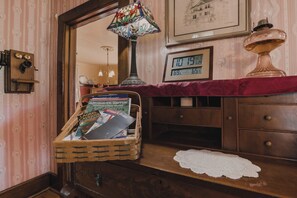 A wooden dresser with a red cloth, a wicker basket with magazines, a clock, and a stained glass lamp.