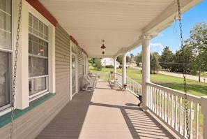 A covered porch with a view of a well-maintained lawn and a distant house.