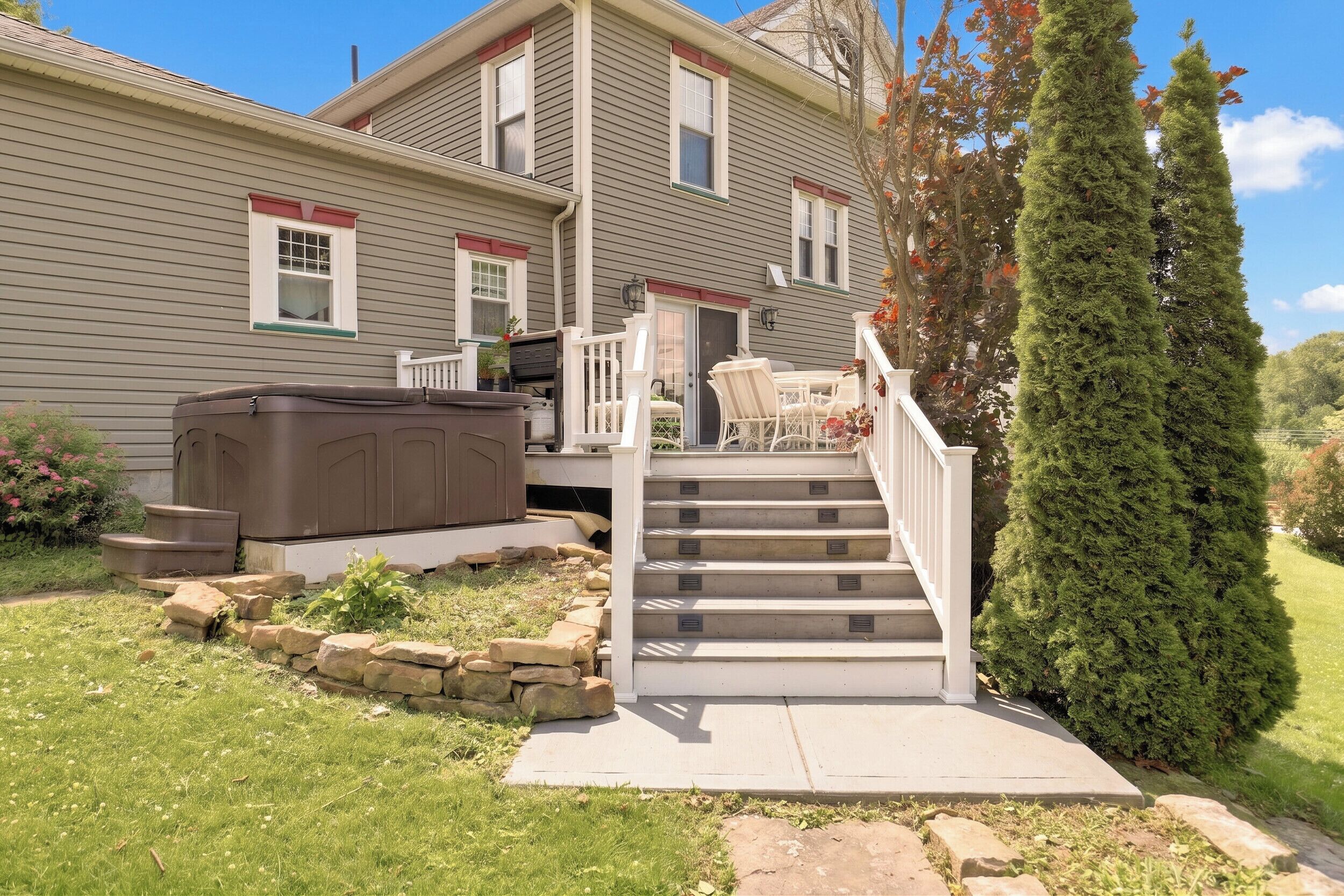 A two-story house with a covered patio, outdoor seating, and a stone staircase leading to the deck.