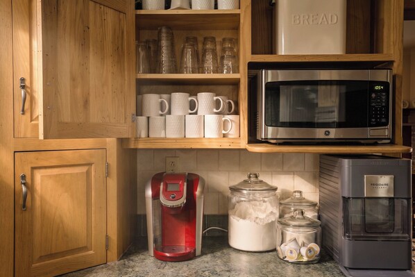 A kitchen with wooden cabinets, a stainless steel microwave, a red coffee maker, and glass jars on the countertop.