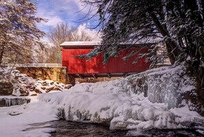 A red covered bridge over a frozen stream with snow-covered trees and a stone wall.