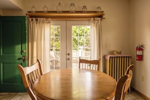 A dining area with a wooden table and chairs, a green door, and a view of the outdoors through a glass door.