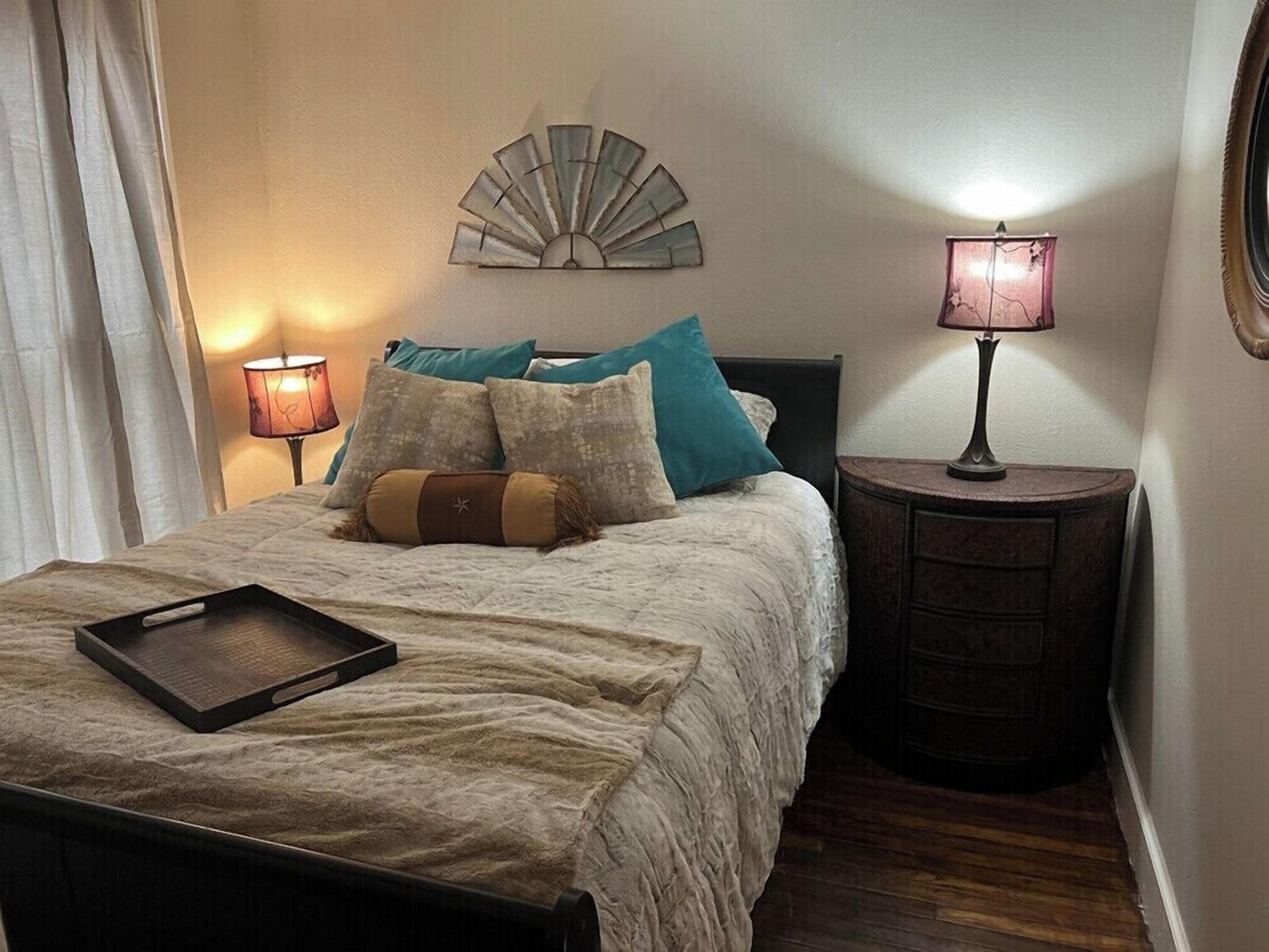 A neatly made bed with a tray, two bedside lamps, and a decorative wall piece.