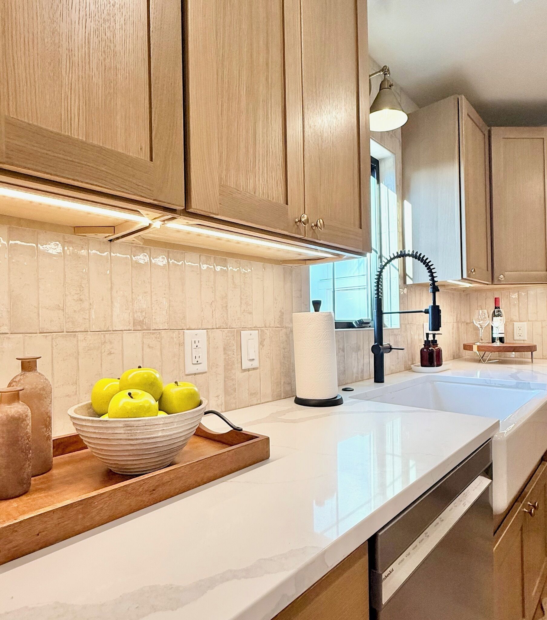 A modern kitchen with wooden cabinets, a white countertop, and a bowl of apples.