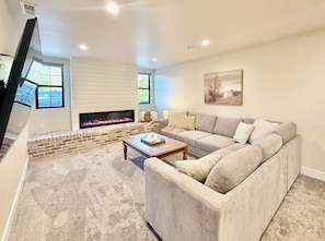 A living room with a fireplace, a sectional sofa, a coffee table, and a television. - The Ayres House, UofO-Autzen • Luxury • Putting Green • Outdoor Living • Hot Tub (Eugene)