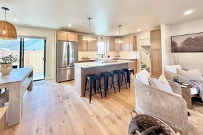 A modern kitchen with a central island, bar stools, and a dining area with a wooden table and chairs. - The Ayres House, UofO-Autzen • Luxury • Putting Green • Outdoor Living • Hot Tub (Eugene)