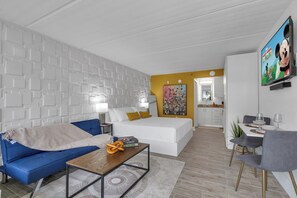 Ein modernes Hotelzimmer mit einem blauen Sofa, einem Holztisch, einem weißen Bett und einer Essecke mit einem grauen Stuhl und Tisch.