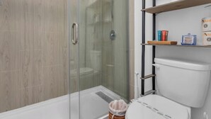 Een moderne badkamer met een douchecabine van glas, een wit toilet en een plank met toiletartikelen.