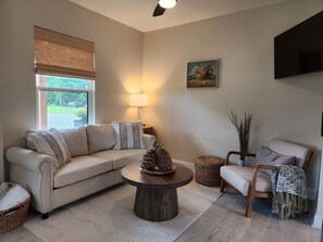 A living room with a sofa, armchair, coffee table, lamp, and a painting on the wall.