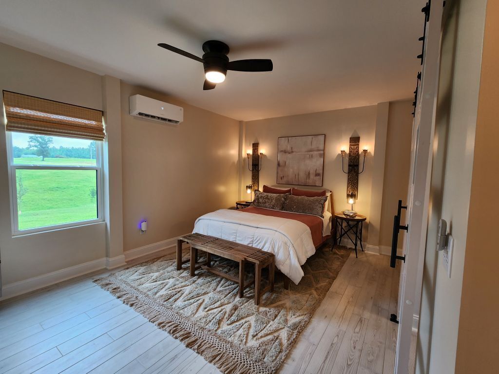 Een slaapkamer met een bed, een plafondventilator, een raam met uitzicht en een wandairconditioner.