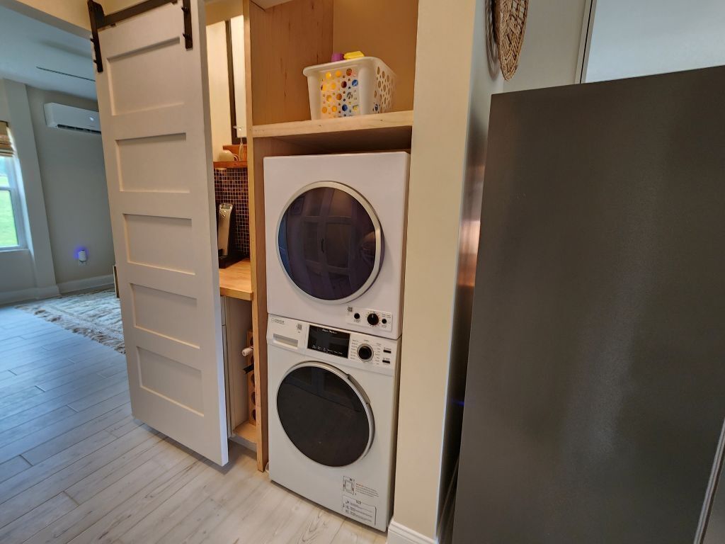 Ein Waschraum mit einer Frontlader-Waschmaschine und einem Trockner, einem Holzbodenregal mit Wäschekörben und einer Schiebetür.