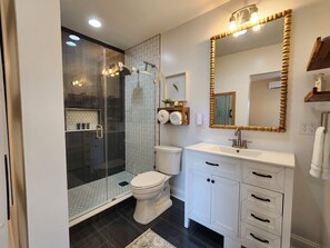 A modern bathroom with a glass-enclosed shower, a toilet, a sink, and a vanity with drawers.