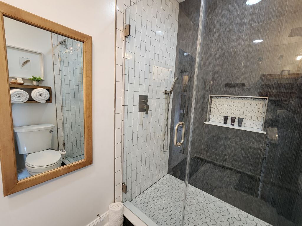 A modern bathroom with a glass-enclosed shower, a white toilet, and a mirror with a wooden frame.