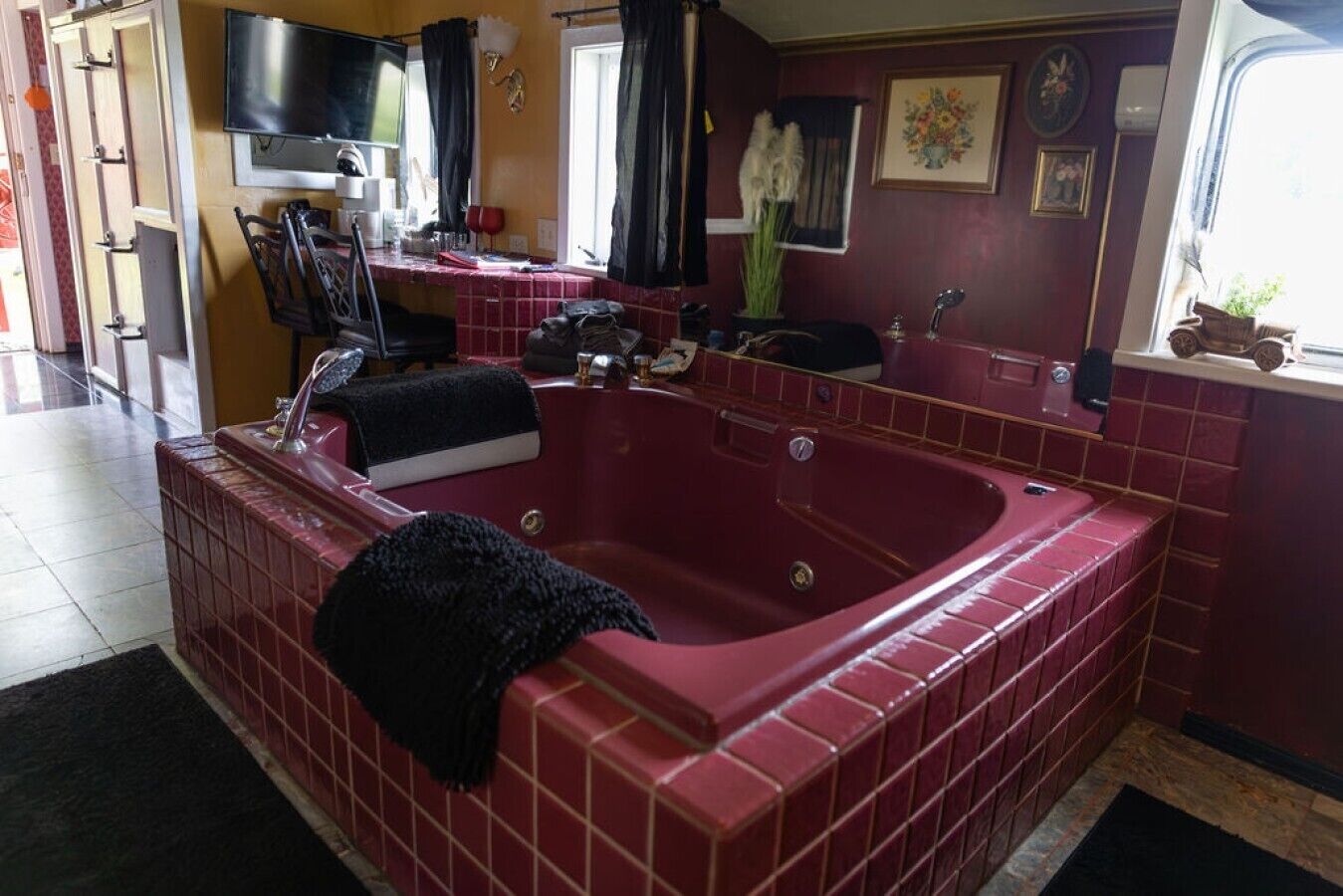 A bathroom with a red bathtub, a sink, a mirror, and a window.