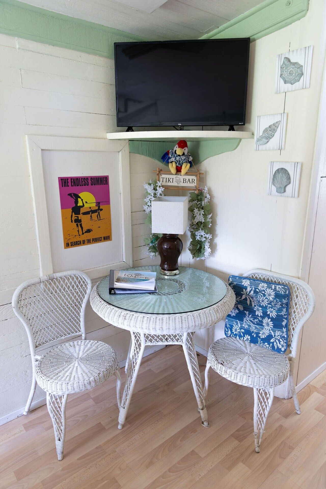 A room with a round glass table, two wicker chairs, a television mounted on the wall, and a poster on the wall.