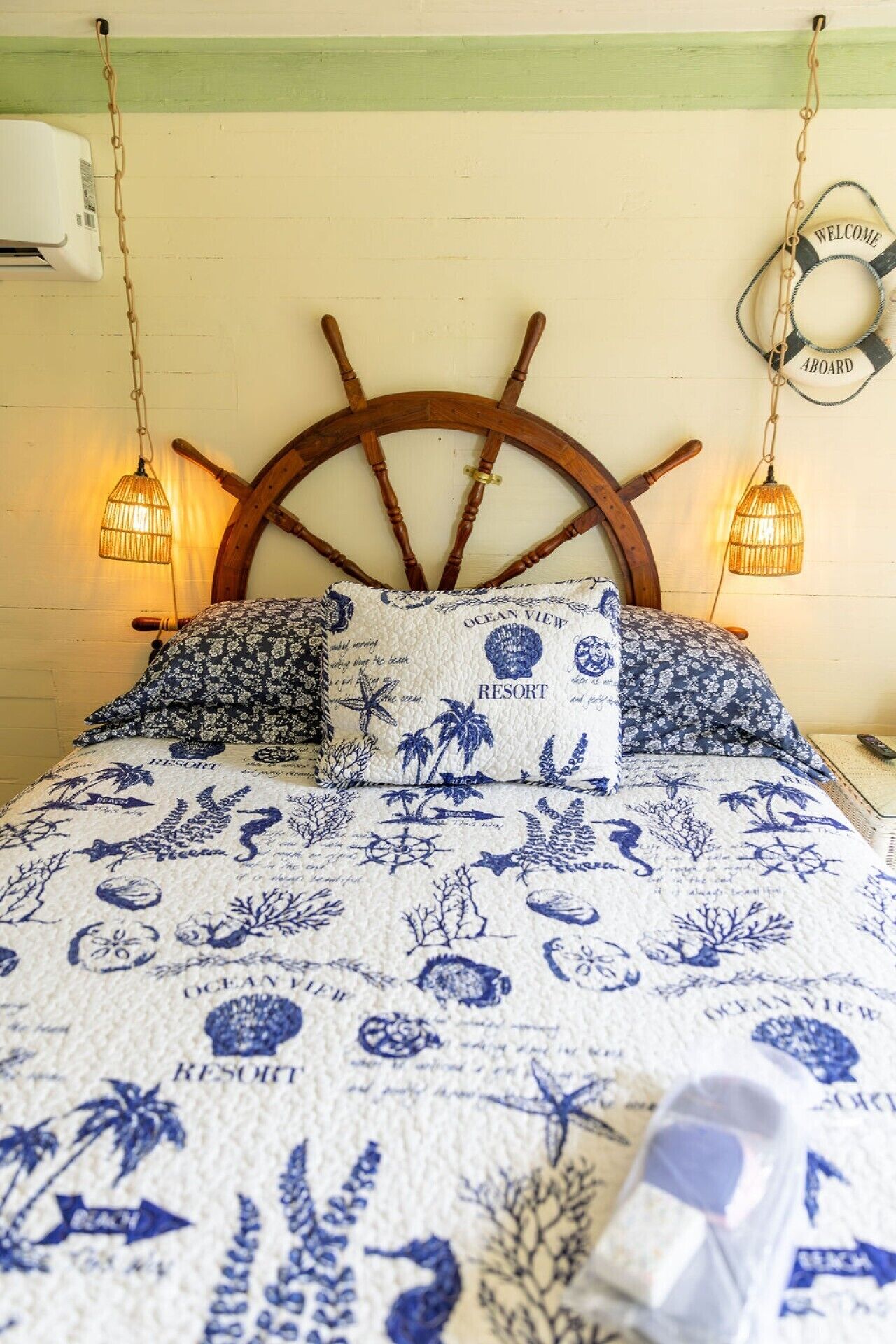 A bed with a nautical-themed headboard, a patterned bedspread, and two wall-mounted lamps.