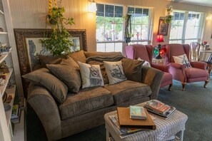 Una sala acogedora con un sofá marrón, una mesita con libros y un sillón rosa.