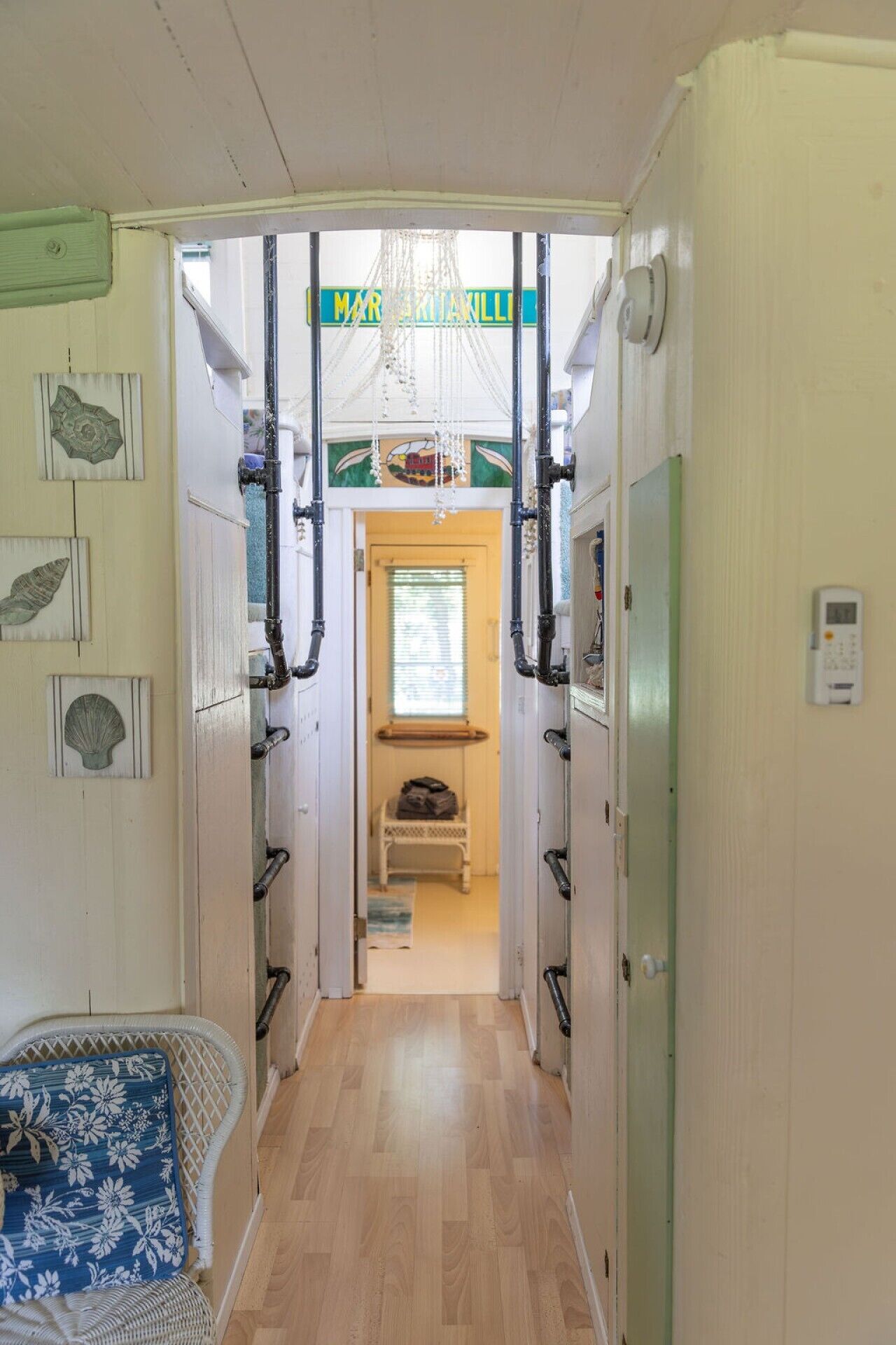 A narrow hallway with a wooden floor, a chair with a floral cushion, and a window with blinds.