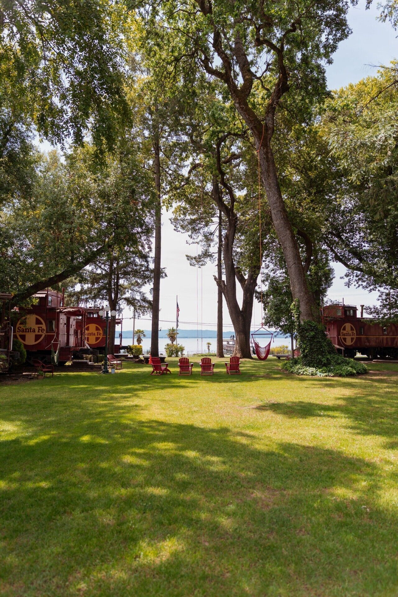 Un espace verdoyant avec des fauteuils Adirondack rouges, un wagon de train rouge et un grand arbre.