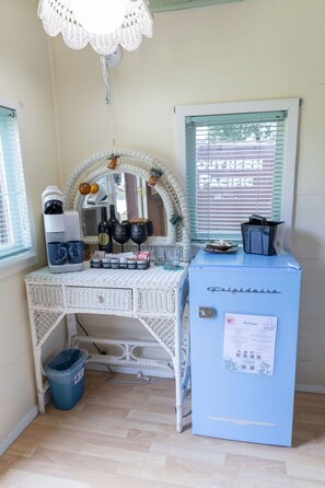 A room with a white wicker desk, a coffee maker, mugs, and a blue cabinet with a welcome sign.