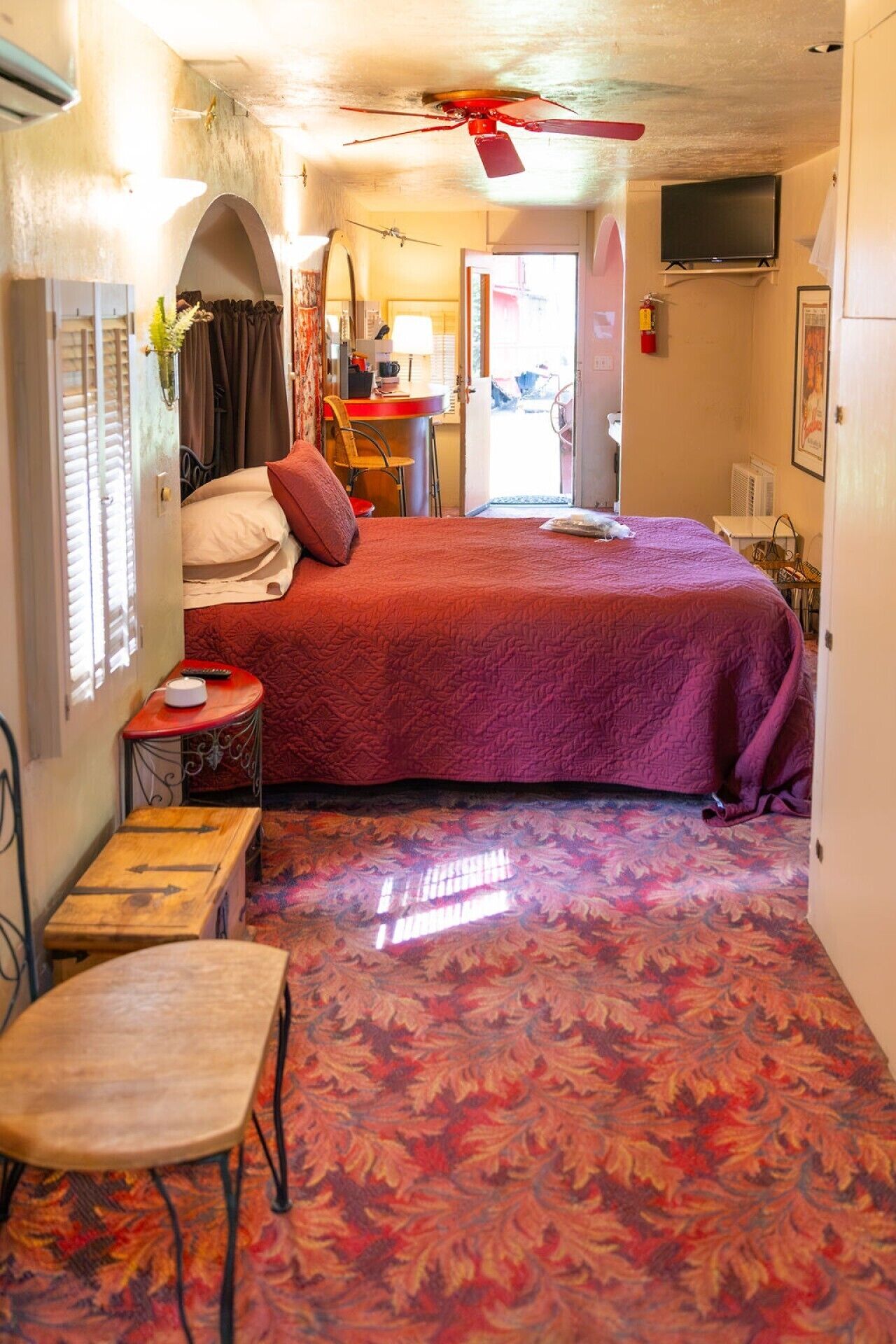 A bedroom with a bed, a desk, a chair, a television, and a ceiling fan.