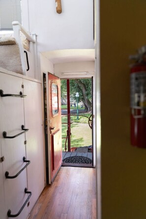 Um corredor com uma porta de madeira que dá para área externa com vista para um parque e um extintor de incêndio fixado na parede.