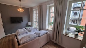 A bedroom with a bed, a TV mounted on the wall, and a window with curtains.