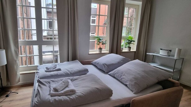 Et hotelværelse med en seng, et natbord, en lampe og et vindue med gardiner.