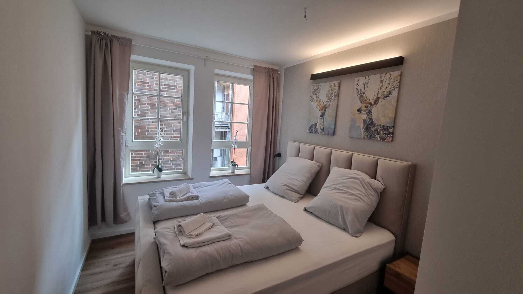 A bedroom with two beds, a window with curtains, and artwork on the wall.