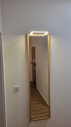 Ein Flur mit einem Spiegel an der Wand, einer Leuchte darüber und einer Tür am Ende.