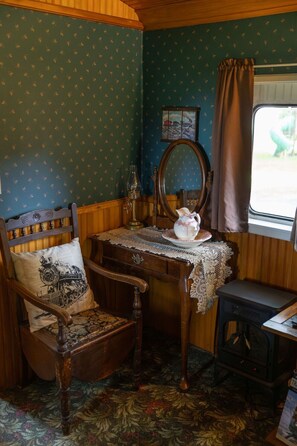 A cozy room with a wooden bed, a table with a lace tablecloth, a vintage radio, and a window with curtains.