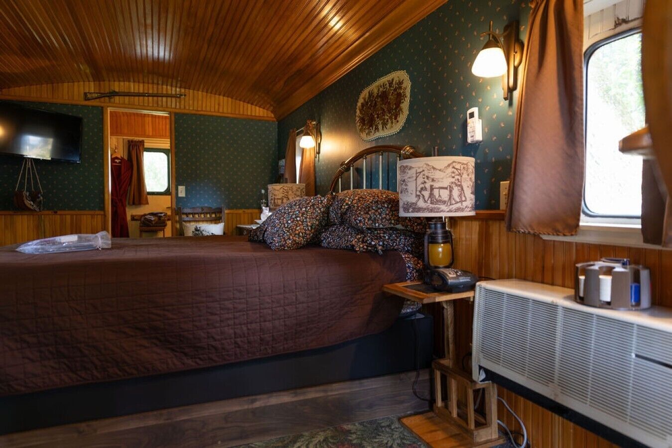 A cozy interior with a large bed, a small table with a lamp, and a window with curtains.