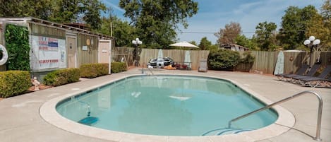 A swimming pool with a metal ladder, surrounded by a wooden fence, and a sign indicating caution.