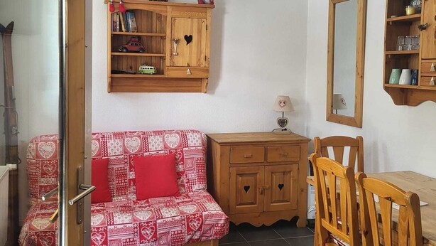 Una stanza accogliente con un divano in legno, un tavolo da pranzo con sedie, un armadietto e una lampada a sospensione.