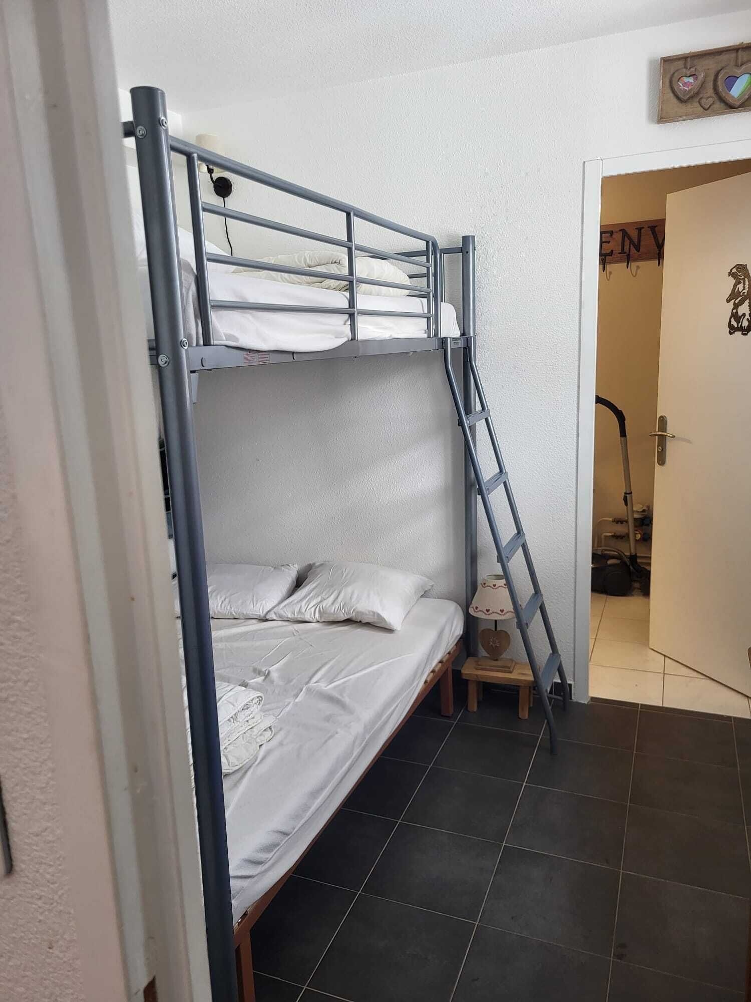 A bunk bed with a ladder, a small bedside table, and a door with a sign.