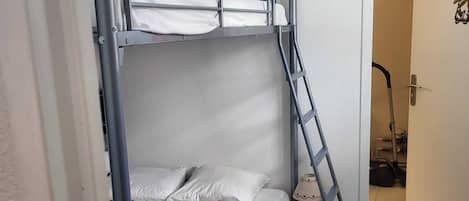 Una cama litera con una escalera, una mesita de noche pequeña y una puerta con un cartel.