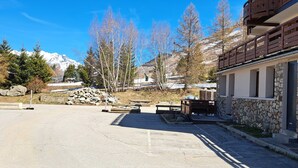 Un edificio in pietra con un balcone, una zona pavimentata con panchine e montagne sullo sfondo.